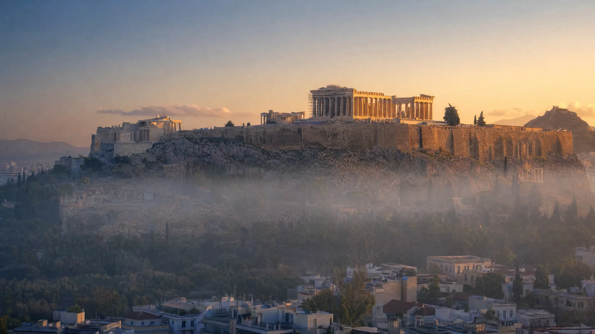 The Parthenon on the Acropolis in Athens lit by golden dawn light, with the city below still in blue shadow and morning mist.