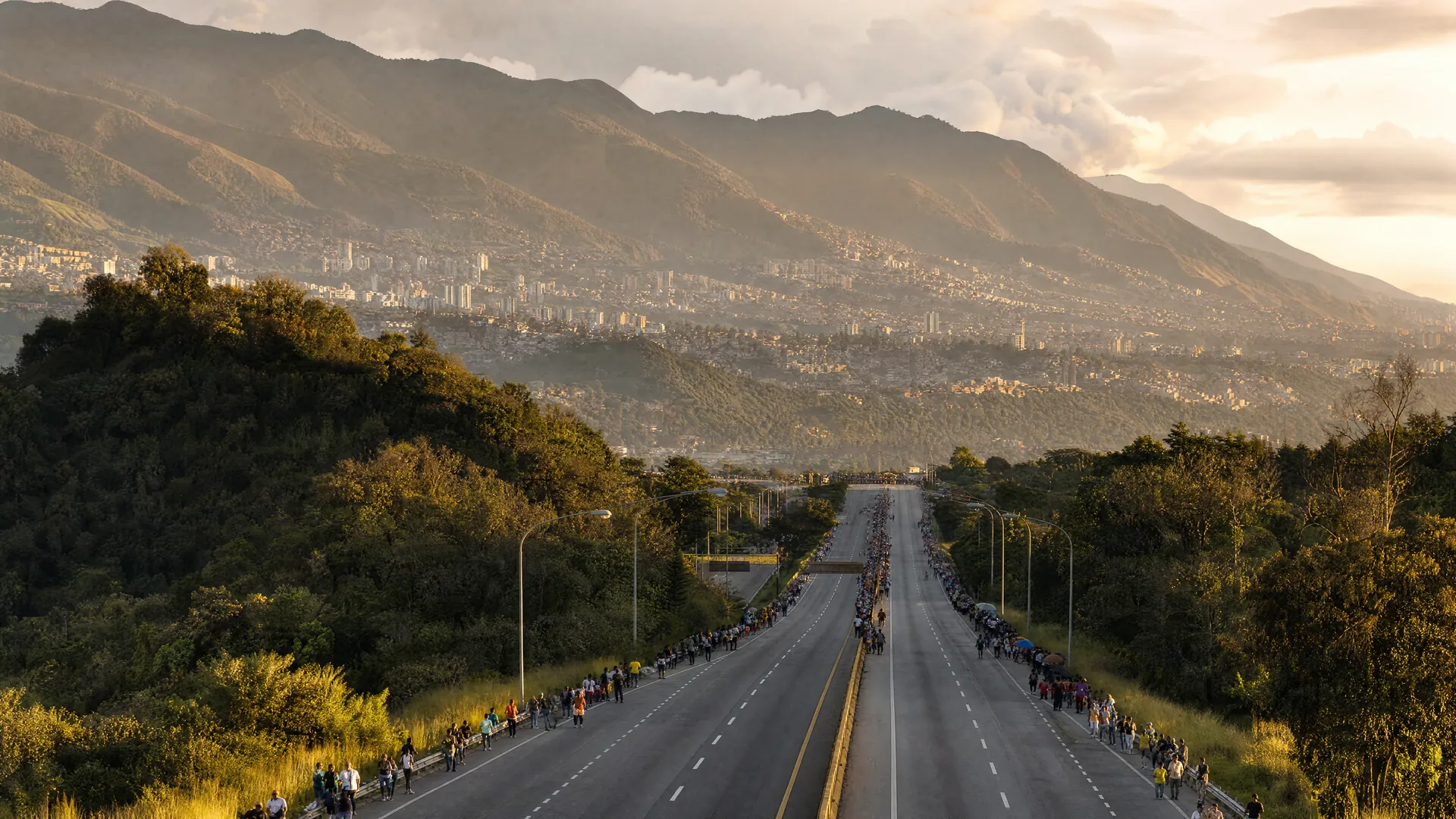 A highway winding through green hills toward Caracas at golden hour, with small distant crowds gathered along the roadside.